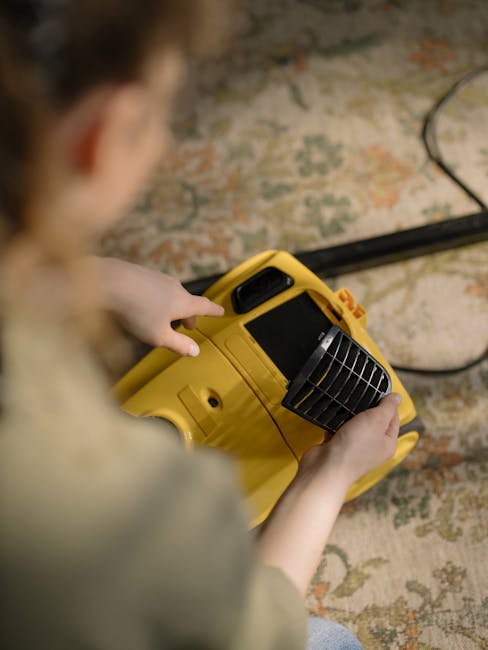 A professional cleaner from Carpet Cleaning W5 is engaged in deep cleaning a beige, plush carpet within a well-lit living room. The cleaner is dressed in a white full-body protective suit, including a